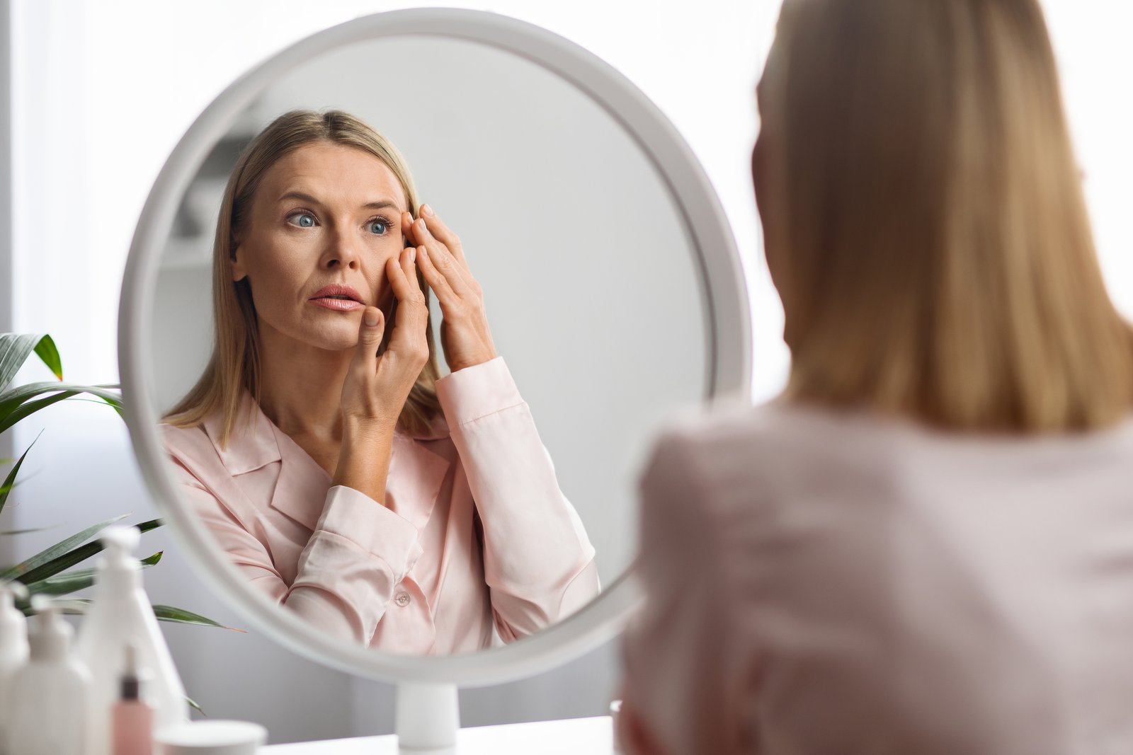 Woman at a vanity mirror examining the skin around her eye