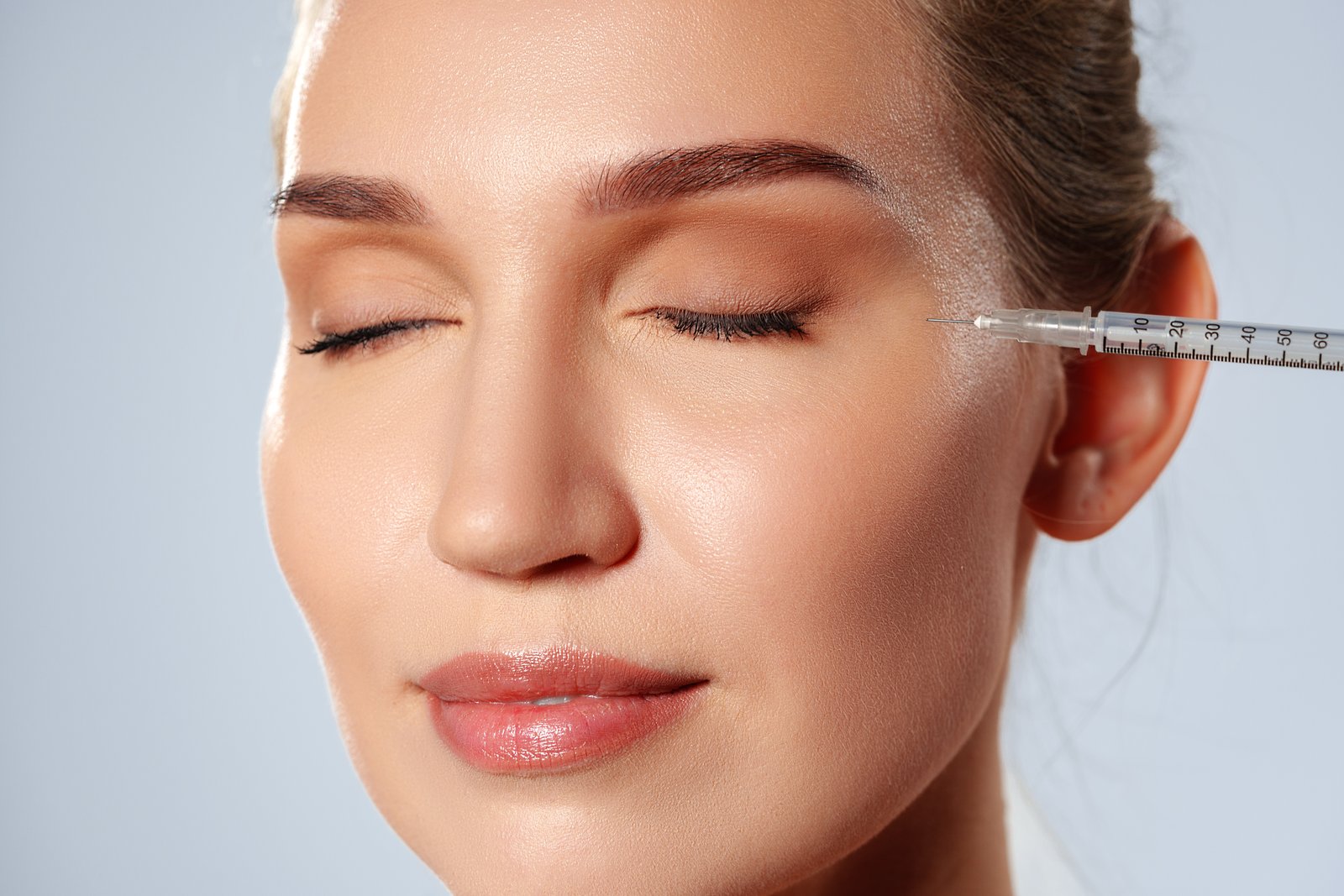 Woman with her eyes closed receiving a cosmetic injection near the temple