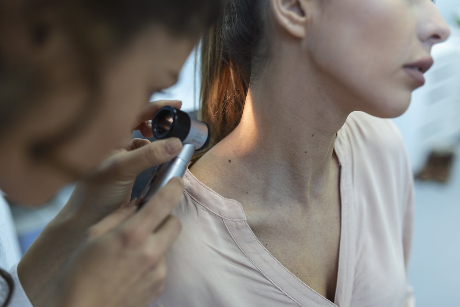 Dermatoscope held to the side of a patient's neck during a skin exam