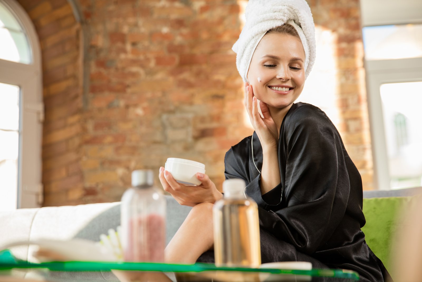 Woman with a towel on her head applying cream from a jar during her skincare routine