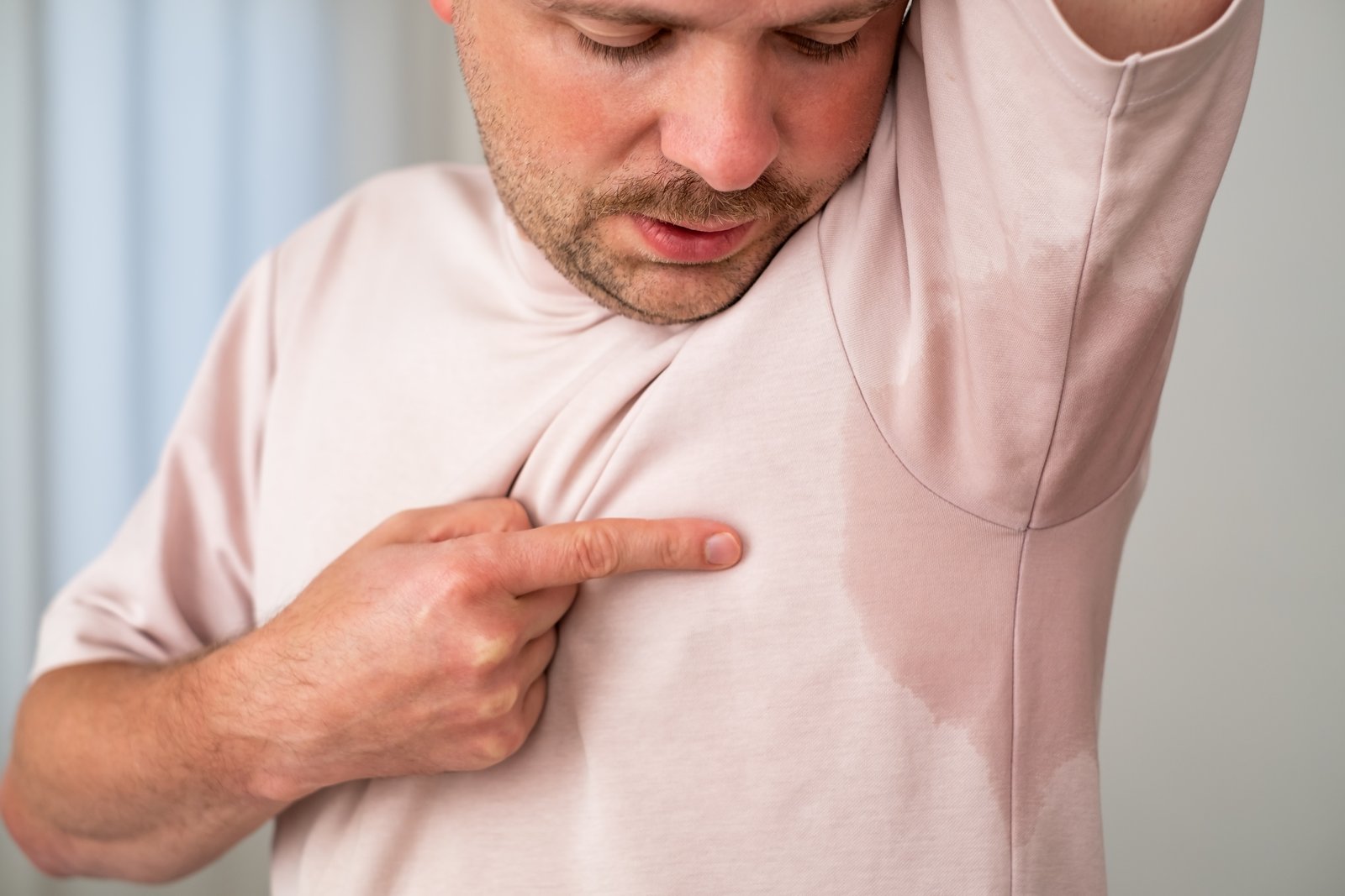Man pointing at a large sweat patch under the arm of his shirt