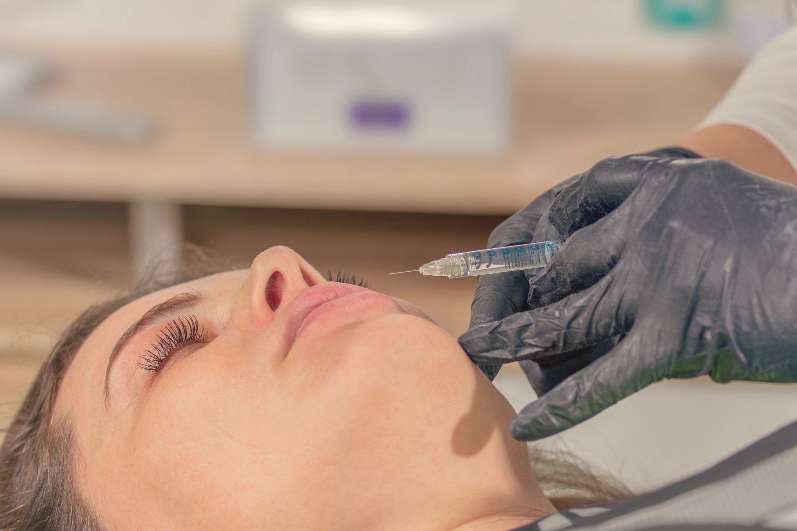 Close-up of a gloved hand giving a lip filler injection to a reclining patient