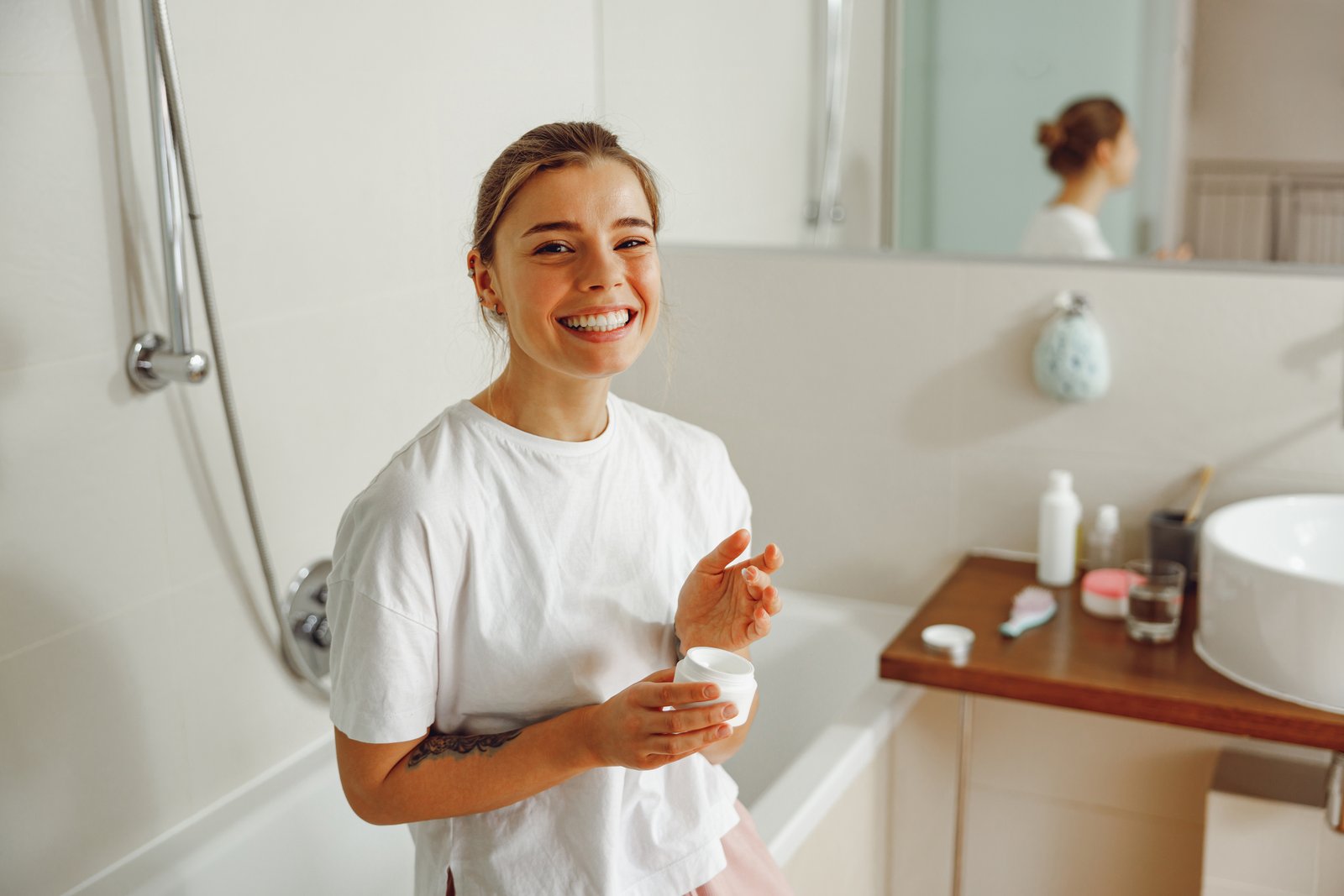 Smiling woman holding a jar of skincare cream in a bathroom