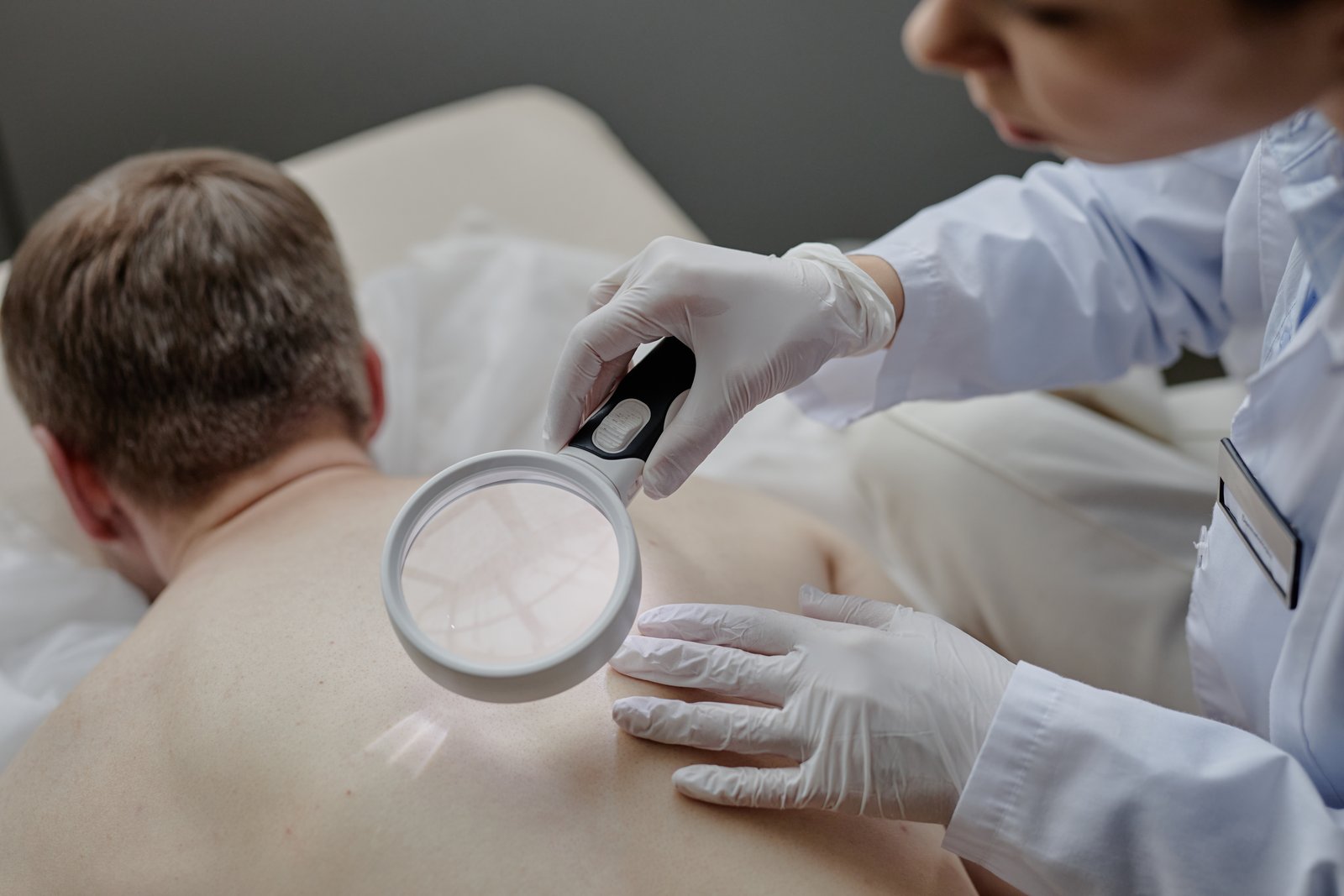Dermatologist examining a patient's back with a large magnifier in a clinic