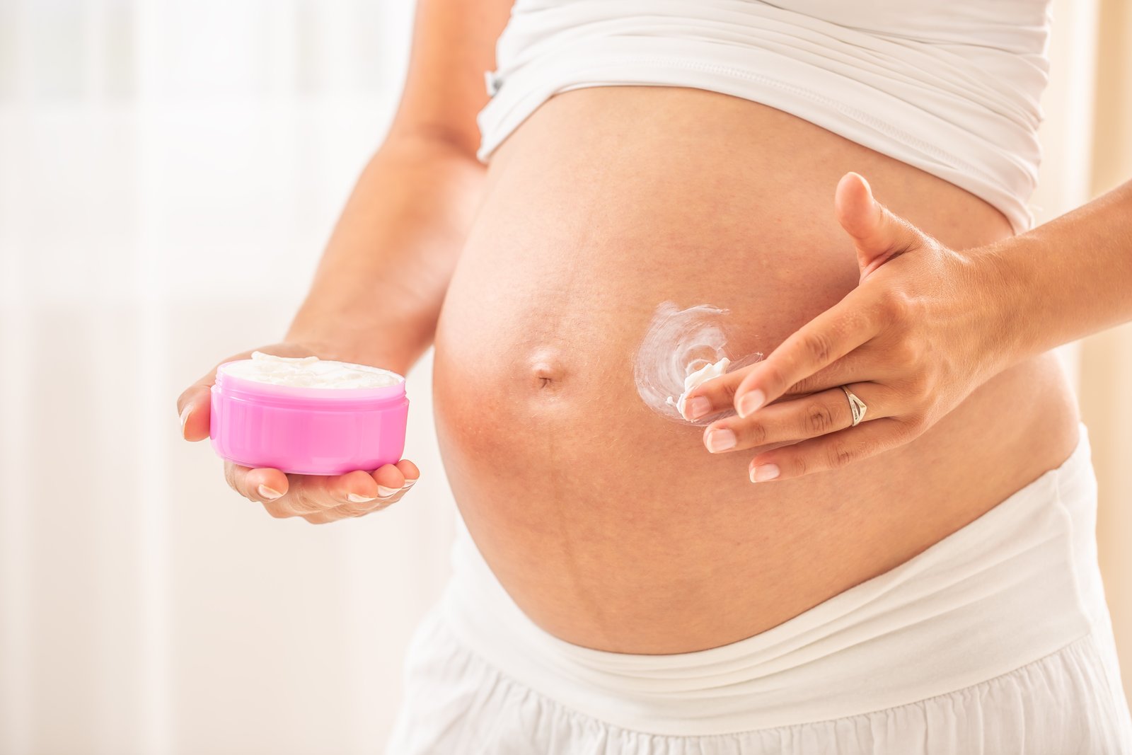 Pregnant woman holding a jar of cream and applying it to her stomach