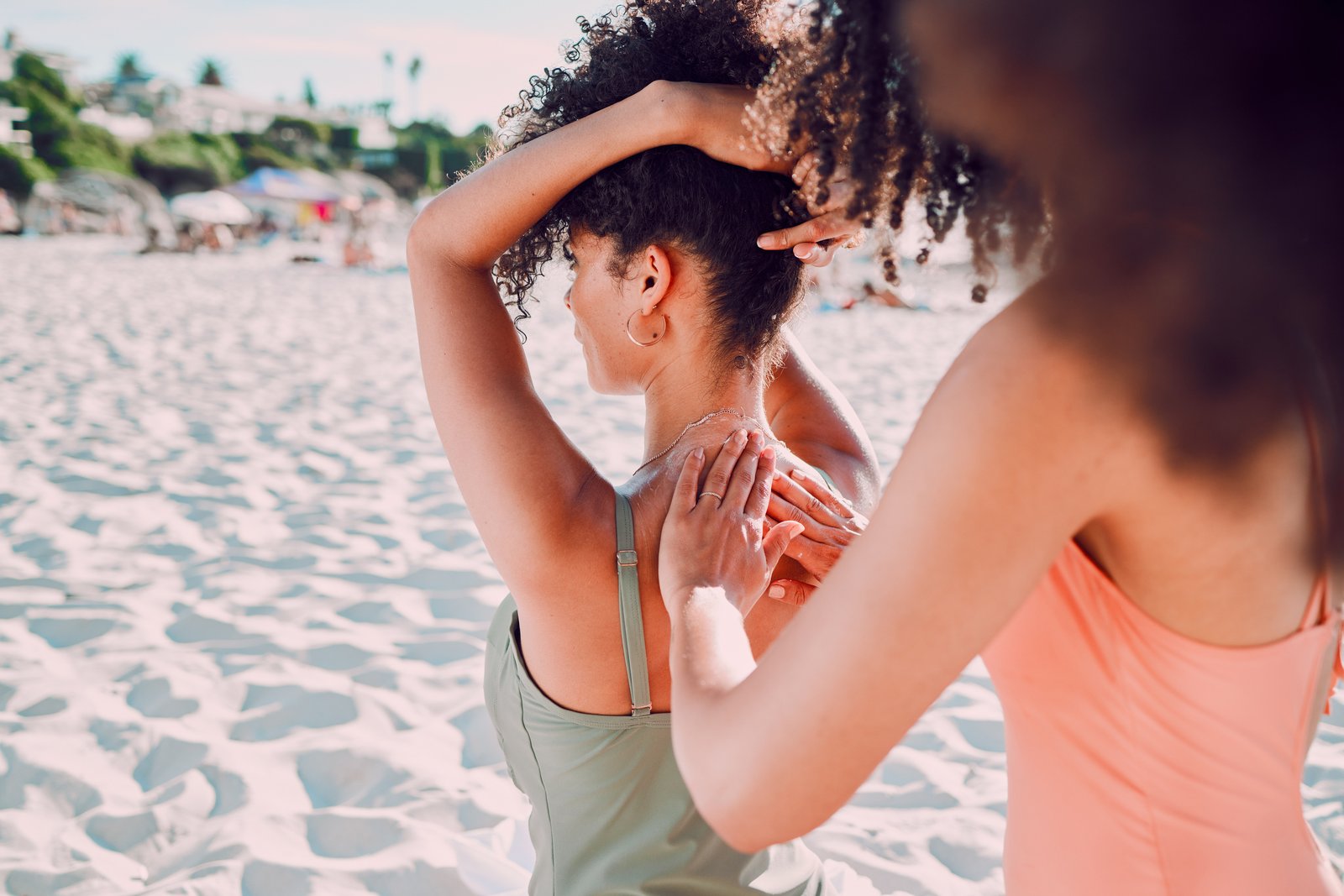 Person applying sunscreen to a friend's shoulders on a sunny beach
