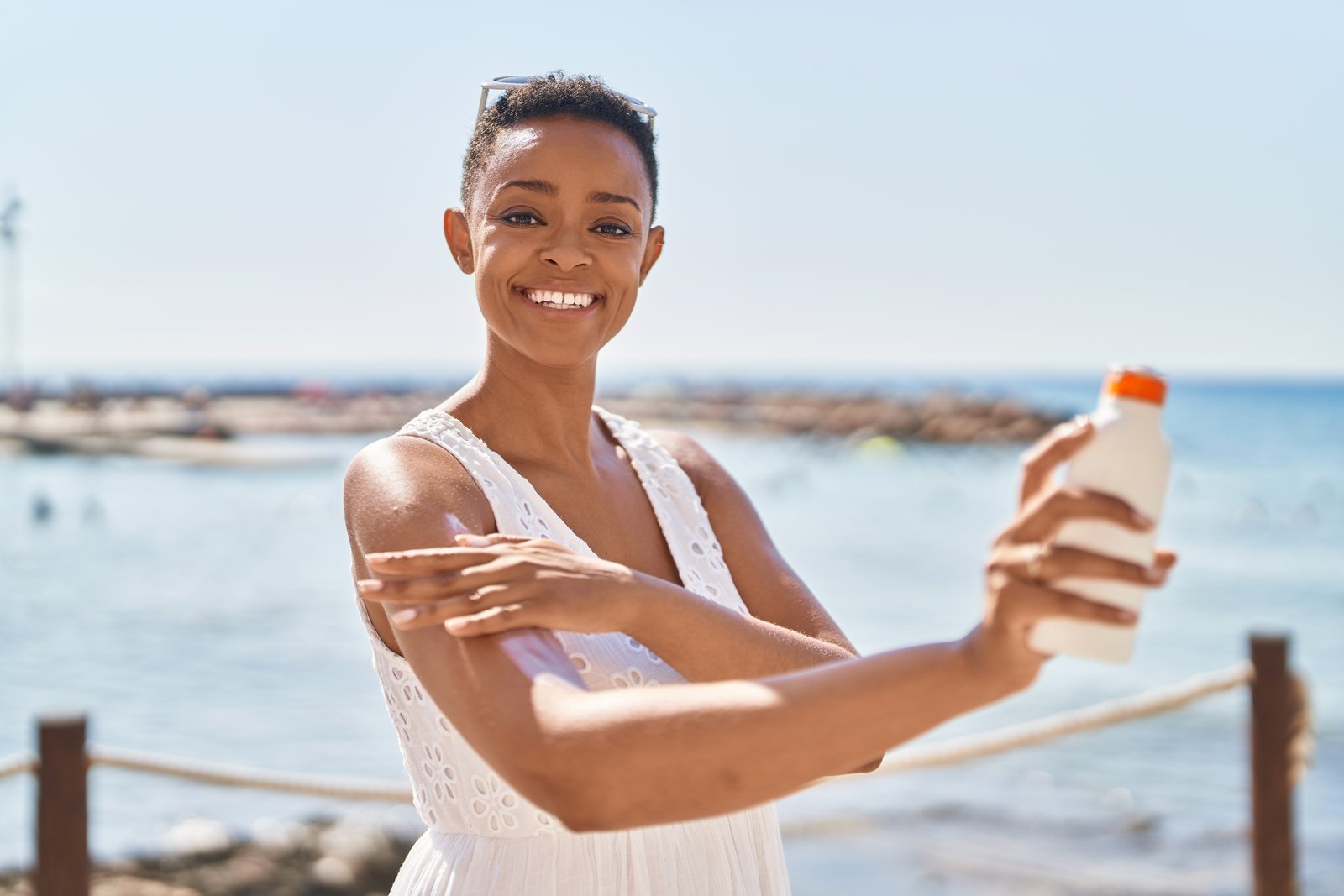 Smiling woman rubbing sunscreen into her arm by the sea