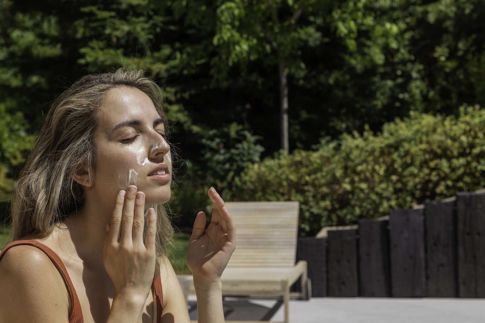 Woman with her eyes closed spreading sun cream over her face outdoors