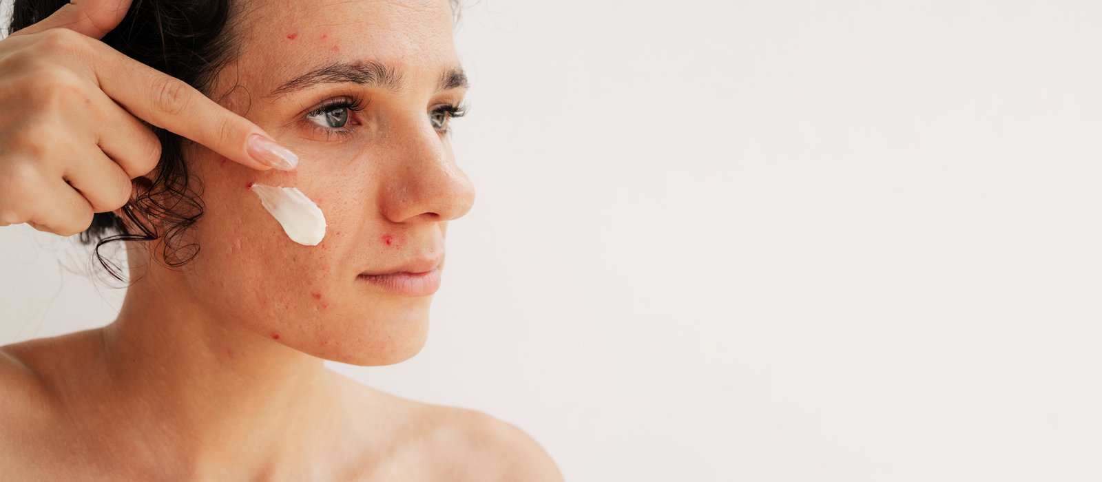 Woman applying a dab of moisturiser to her cheek