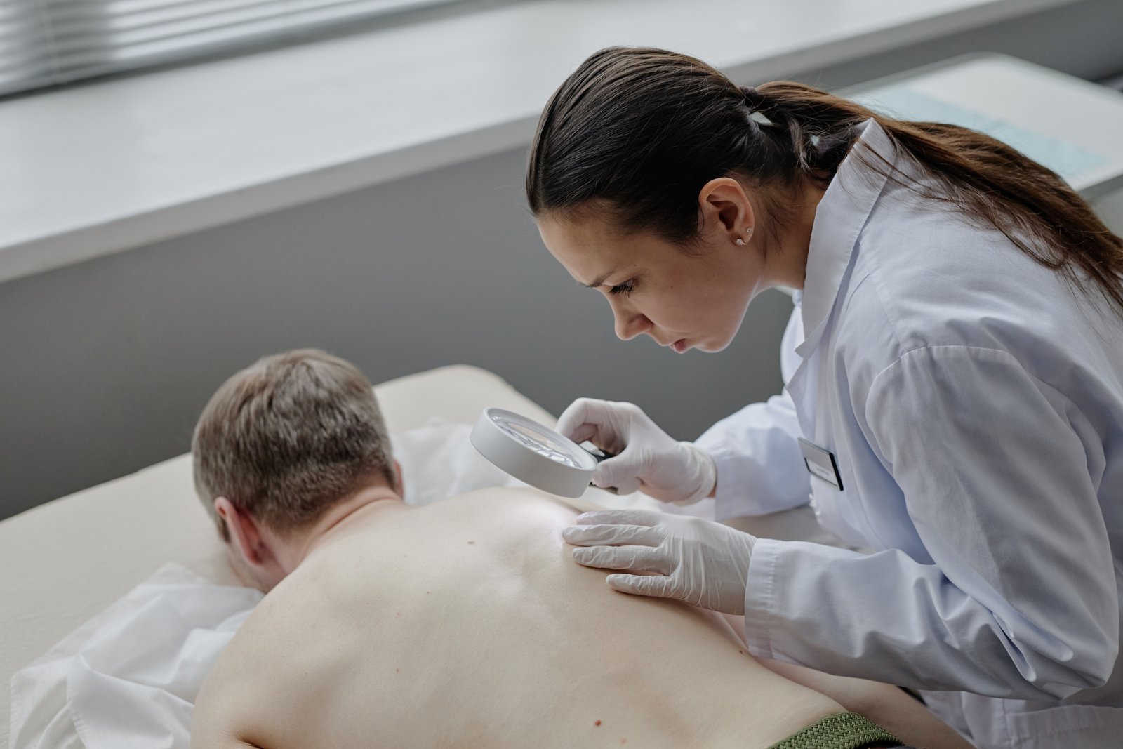 Dermatologist in a white coat examining the back of a man lying on an exam table