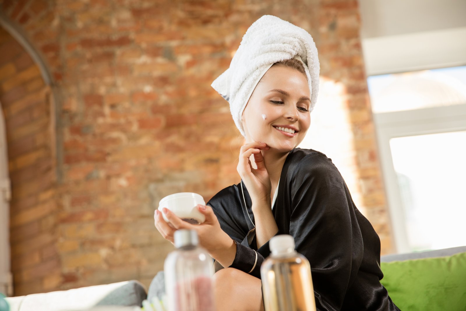 Woman in a robe with a towel on her head holding a jar of face cream