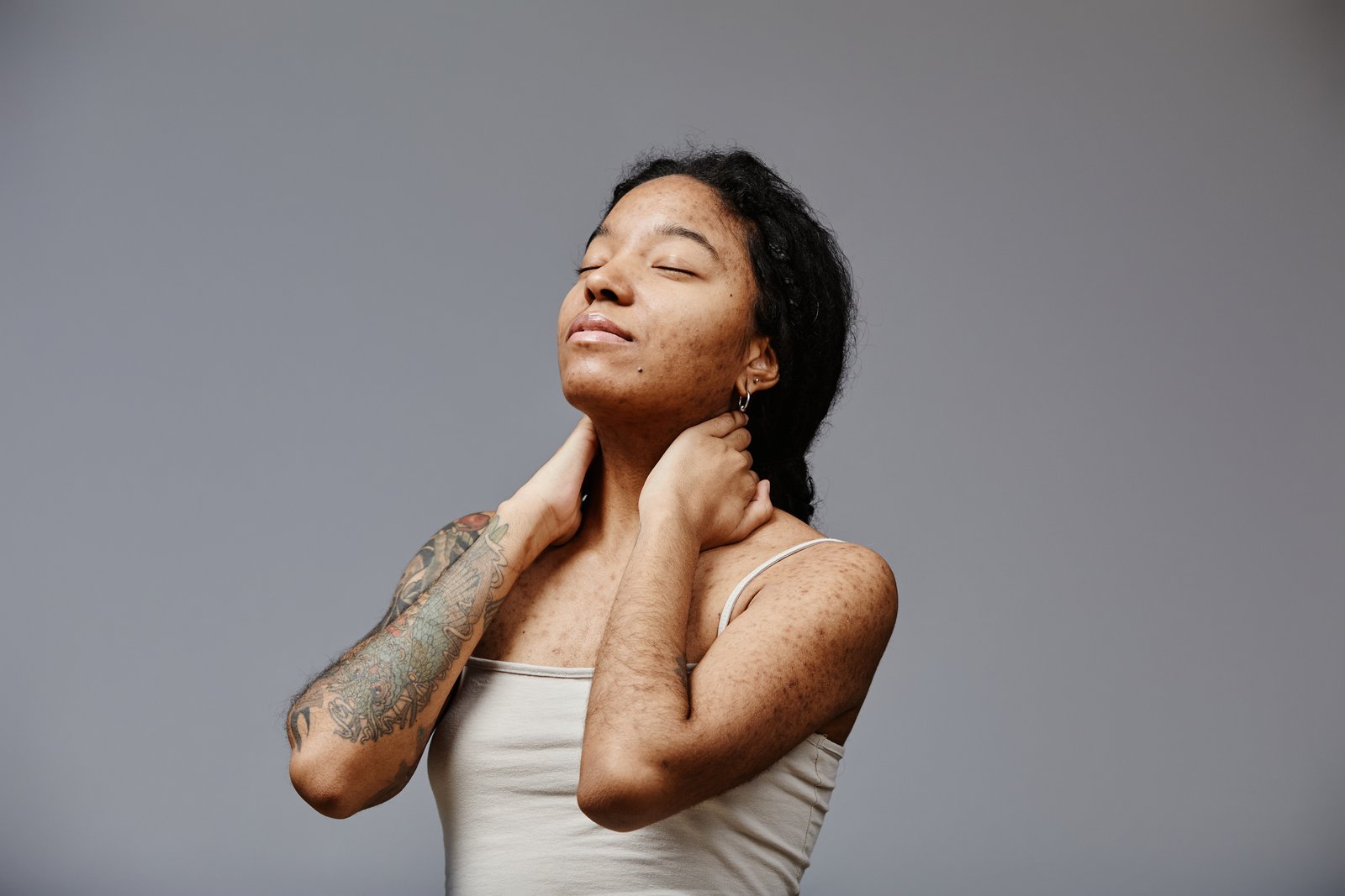 Woman in a white tank top tilting her head and touching the side of her neck