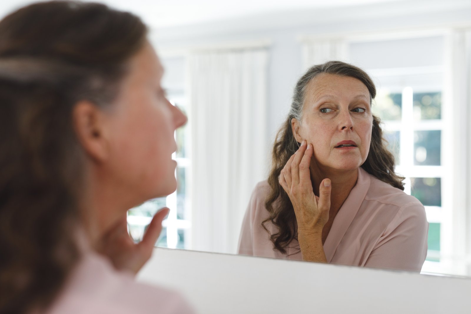 Woman examining the skin on her cheek in a bathroom mirror