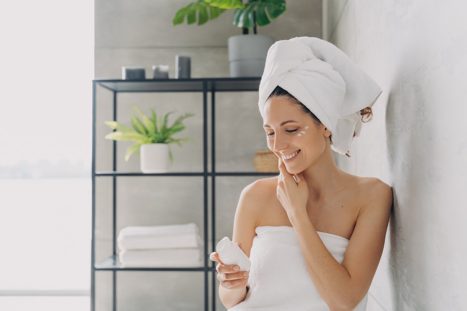 Woman wrapped in a towel applying moisturiser in a bathroom
