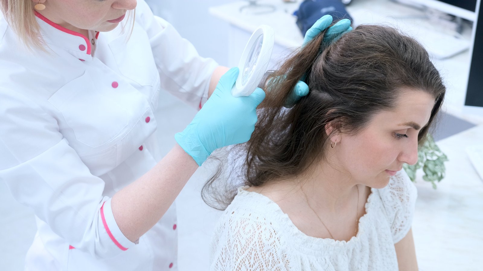 Gloved clinician parting a patient's hair to examine the scalp
